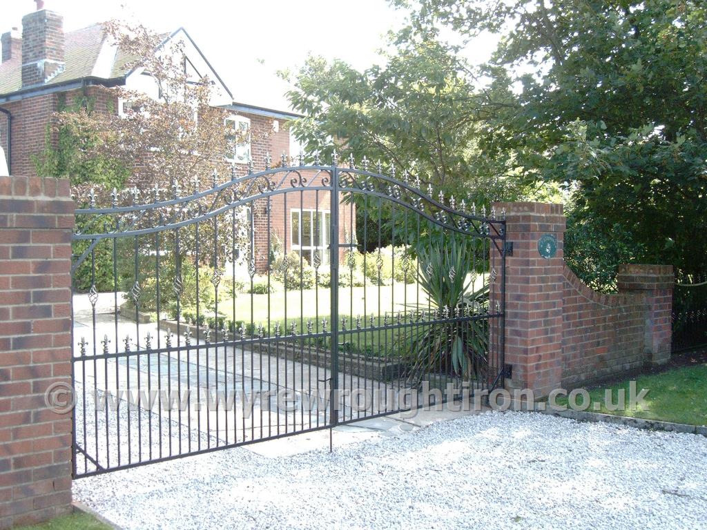 Imposing wide and tall double arched driveway gates with scrollwork, railheads, cage twists and black finish, fitted to a house in Hambleton, Over Wyre.